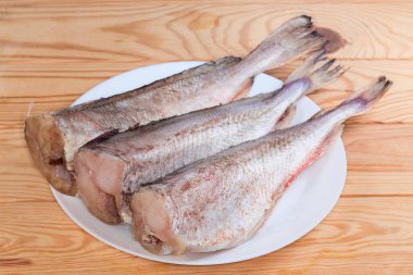 Kafası olmayan kırmızı morina leşleri, beyaz tabakta balık pullarından temizlenmiş ahşap bir kırsal masada, seçici bir odak noktasında yan görüş