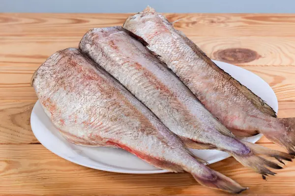 Cooled carcasses of the red cod without heads, cleared from fish scales on white dish on a wooden rustic table, side view in selective focus