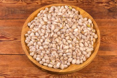 Heap of the roasted salted pistachio nuts with partly naturally open shells on a big wooden dish on the old rustic table close-up clipart