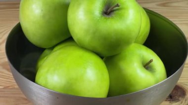 Kırsal bir masada metal kasede yeşil elmalar.