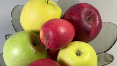 Elmalar gri arka planda cam meyve kasesinde farklı renkte.