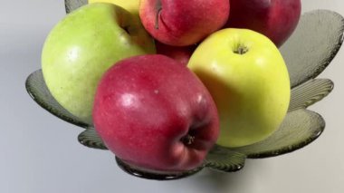 Elmalar gri arka planda cam meyve kasesinde farklı renkte.