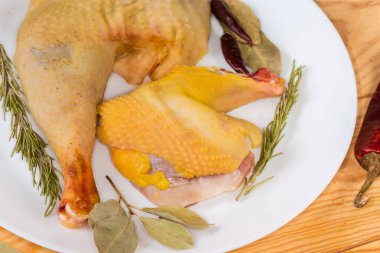 Raw leg and shoulder of rooster grown on the farm by free range method outdoors with yellow skin among the different dry spices on dish on a rustic table, fragment close-up clipart