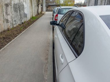 Yan taraflarında farklı arabaların yan aynaları var. Kaldırıma yakın bir sıraya park edilmiş. Bulutlu bir bahar sabahı beton istinat duvarına yaslanmış.