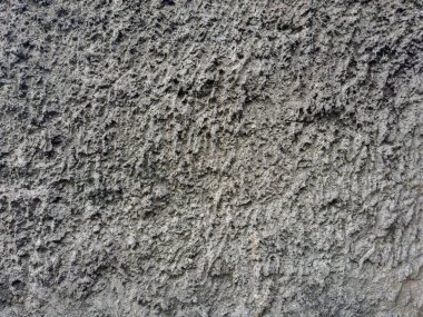 Eski duvarın, gri çimentoyla kaplanmış kabataslak dekoratif yardım alçısıyla kaplı parçası, bulutlu havada açık hava manzarası.