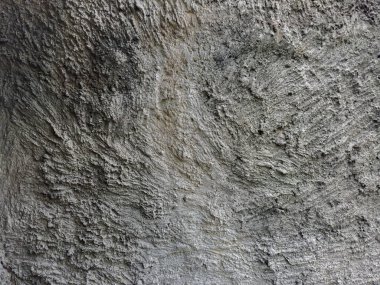 Eski duvarın, gri çimentoyla kaplanmış kabataslak dekoratif yardım alçısıyla kaplı parçası, bulutlu havada açık hava manzarası.