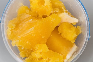 Gri arkaplan üzerinde açık plastik kabın içinde kristalize edilmiş beyaz bal parçaları, yakın çekim parçasının üst görüntüsü