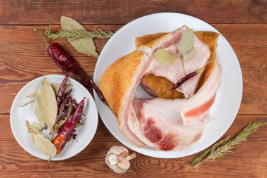 Tuzlanmış domuz eti parçaları derinin üstünde et katmanları beyaz tabakta farklı baharatlar arasında ve kırsal bir masada taze sarımsak, üst görünüm.