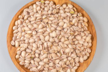 Bir yığın kavrulmuş tuzlu şam fıstığı kısmen açık kabuklu büyük ahşap bir çanakta gri arka planda, yakın plan üst görüntü