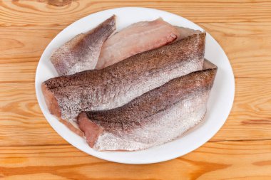 Kırsal masadaki beyaz bir tabakta, deride çözülmüş hake filetoları.