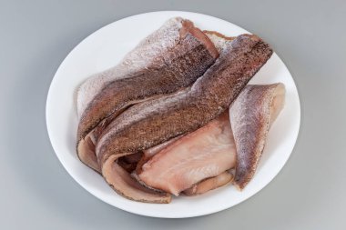 Gri arka planda beyaz bir tabakta, deride çözülmüş hake filetoları.