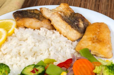 Kızarmış hake fileto parçaları haşlanmış sebzelerle garnitür karışımı ve pilav beyaz bir tabak üzerinde bambu yeri paspası, yakın plan.