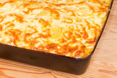 Pişirme tepsisindeki taze sebze güvecinin üstünde kısmen erimiş peynir, seçici odak noktasında parça parça.