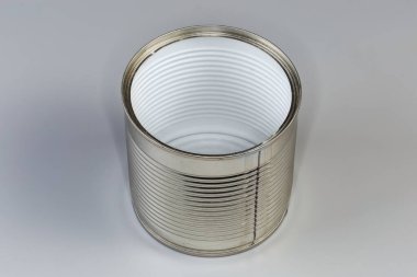 Open empty tin can from under a canned food, lined with white plastic film on the inside on a gray background clipart