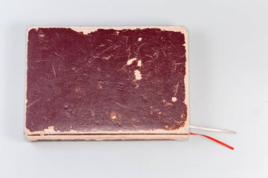 Eski bir kitap, eski bir kırmızı-kahverengi kapağı ve iki okuma kurdelesi var. Gri bir arka planı var.