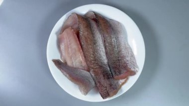 Gri arkaplanda beyaz tabakta çözülmüş çiğ hake filetoları