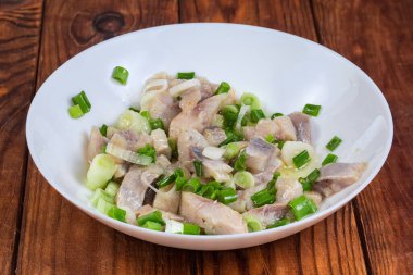 Dilimlenmiş Atlantik Ringa filetosu, doğranmış yeşil soğanla, kırsal bir masada yemek yağıyla tatlandırılmış.