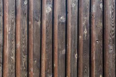 Dikey olarak yerleştirilmiş tahta levhalar ve tahtalarla örülmüş, zamanla kararmış, güneşli havalarda manzaralı eski binanın yüzeyi.