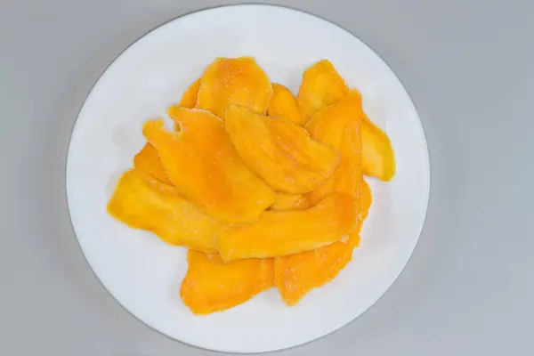 stock image Dried slices of mango pulp on white dish on a gray background, top view