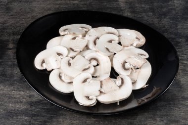 Siyah bir yüzey üzerinde siyah bir tabakta taze çiğ mantar dilimleri.