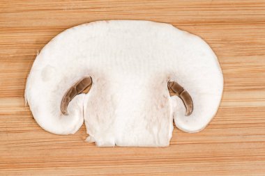 Taze çiğ mantarın ince bir dilimi ahşap bir kesme tahtasıyla boydan boya kesilmiş, üst tarafı yakın plan.