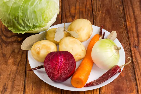 stock image Set of the raw fresh peeled vegetables, white cabbage and dried spices, as ingredients for red beet borscht preparation on a rustic table