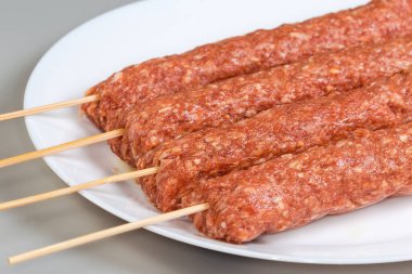 Birkaç çiğ soğutulmuş lula kebabı tahta bambu şişlerinin üzerinde gri bir arka planda beyaz bir tabakta, seçici odak noktasında küçük parçalar halinde.