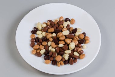 Gri arka plandaki beyaz tabakta siyah, beyaz ve sütlü çikolatalarla kaplı kuru üzüm şeklinde şekerlemeler