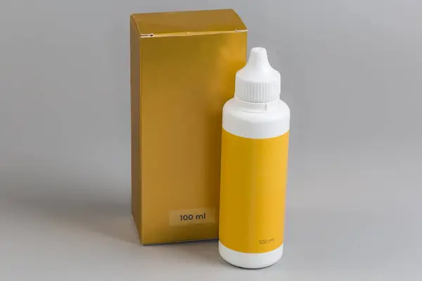 Stock image Closed plastic yellow bottle of liquid pharmaceutical product against the its cardboard box package with indicating volume on a gray background