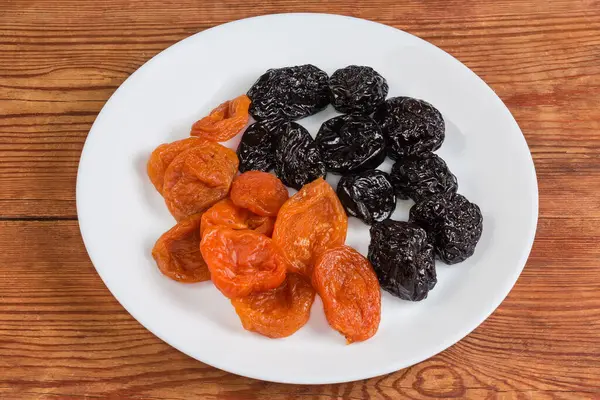 stock image Dried apricots and dried plums on the white dish on a rustic table