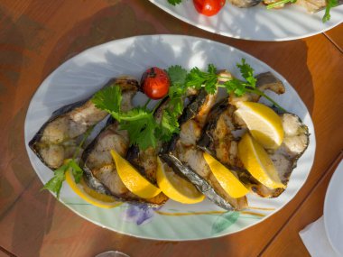 Limon dilimleri ve tabakta kişniş dallarıyla taze Sibirya mersinbalığından ızgara biftekler.