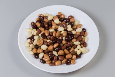 Gri arka plandaki beyaz tabakta siyah, beyaz ve sütlü çikolatalarla kaplı kuru üzüm şeklinde şekerlemeler