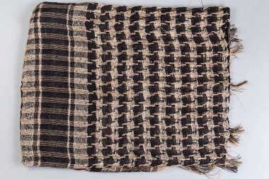 Katlanmış pamuklu bej, kenarlarında püskülleri olan siyah keffiyeh, boynunda ya da başında taktik koruyucu eşarp olan, gri arka planda üst görünümü olan.