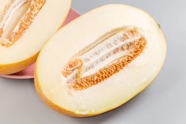 stock image Two halves of ripe fresh yellow melon with seeds and netted skin, cut along on a gray background, close-up 