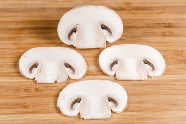 Taze çiğ mantarın ince dilimleri ahşap bir kesim tahtasının üzerinde boydan boya kesilmiş.