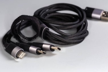 USB-C, mikro-USB ve Lightning sarmalanmış siyah örgülü kablo adaptörünün kenarlarında gri bir arkaplanda, seçici odak noktasında yakın plan