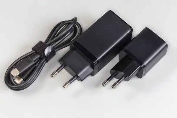 stock image Two black chargers of different power with AC Europlugs for batteries charging of portable electronic accessories and output appropriate cable beside on a gray background