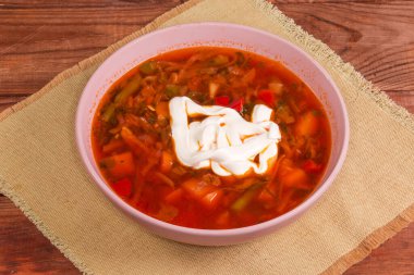 Kırsal bir masada pembe kasede ekşi kremayla tatlandırılmış tipik Ukrayna pancarı servis ediliyor.