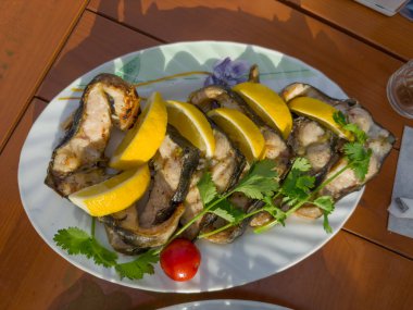 Limon dilimleri ve tabakta kişniş dallarıyla taze Sibirya mersinbalığından ızgara biftekler.