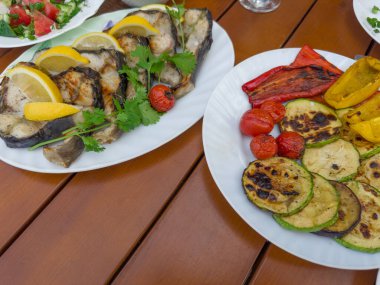 Limon dilimli ızgara biftekler ve tabakta kişniş dalları, taze sebze salatası, masada fırınlanmış sebzeler, üst manzara.