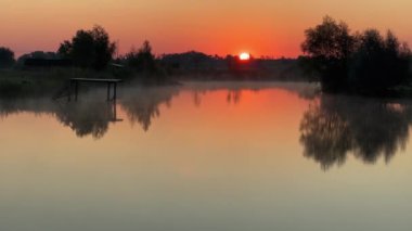 Durgun suyla göl ve yaz gündoğumu boyunca yükselen sis
