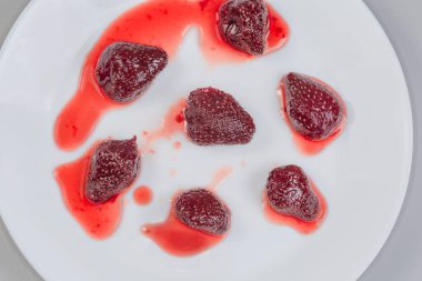 Whole berries of the strawberry jam on the white dish on a gray background, top view clipart