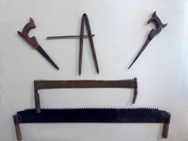 Farklı eski paslı iki adam testereleri ve farklı boyutlarda ve beyaz duvarda asılı diş şekilleri olan çapraz testere.