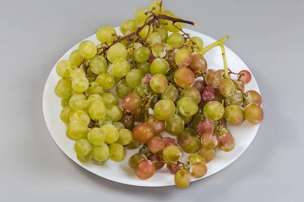 stock image Clusters of the ripe pink and white sultana table grape on a white dish on a gray background