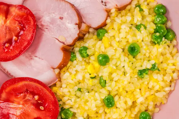 stock image Fried rice mixed with eggs and green peas serving with slices of boiled smoked pork belly and fresh tomato halves in the pink bowl, top view of fragment in selective focus