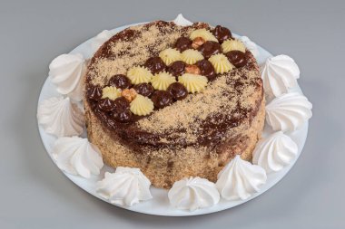 Süt ve beyaz çikolatayla süslenmiş yuvarlak süngerli kek. Gri arka planda, tabakta kremalı kurabiyelerle çevrili.