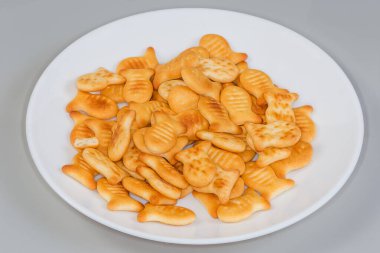 Gri arka planda beyaz bir tabakta küçük balık şeklinde tuzlu kraker yığını.