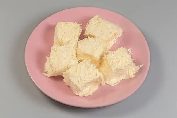 stock image Traditional Turkish sweets pishmanie in form of the pieces of pressed floss made of flour with pulled sugar on a pink dish on a gray background