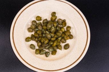 Turşu turşusu, kristalize edilmiş beyaz beneklerle kaplı bir fincan tabağı üzerinde, siyah arka planda üst görünüm.