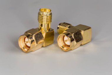 Gri bir yüzey üzerinde erkek ve kadın SMA konnektörleri olan iki yüksek frekanslı sağ açılı eş eksenli sarı pirinç.
